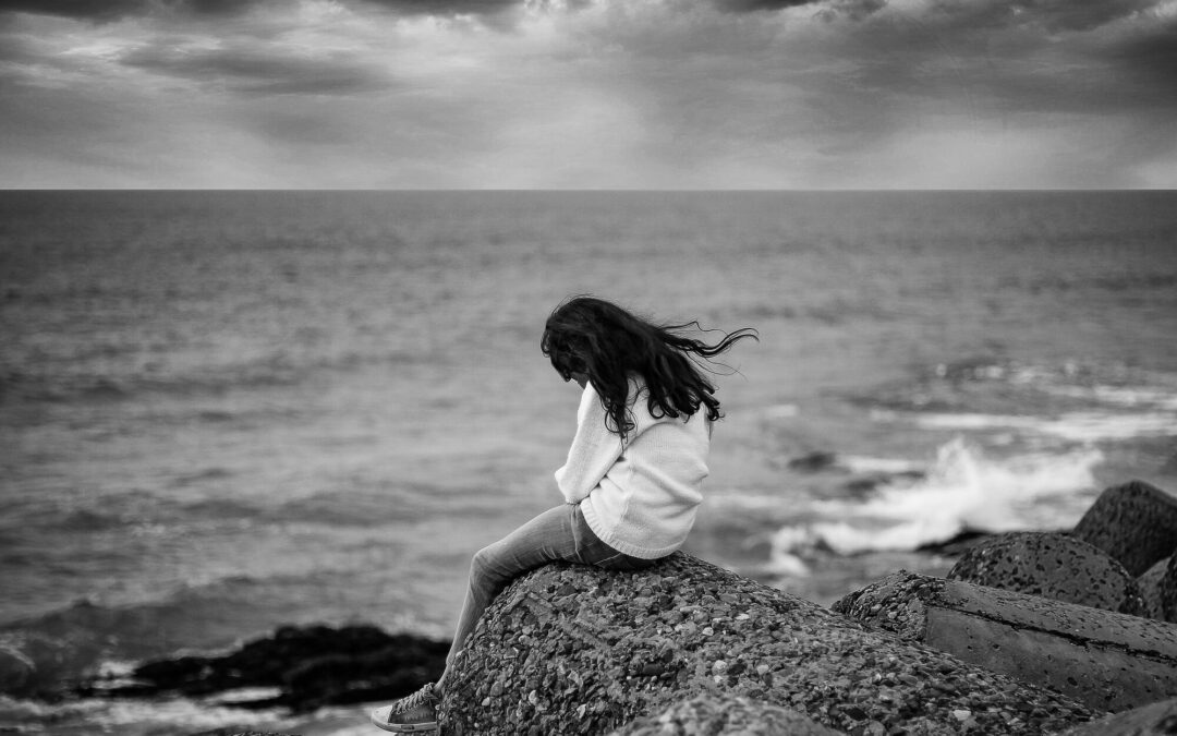 Photo noir et blanc de femme dos assise sur un rocher face à la mer
